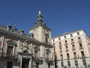 A historic building with baroque architecture under a bright blue sky, next to a modern