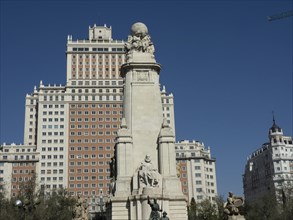 An imposing monument with ornate sculptures and surrounding modern architecture, all under a clear