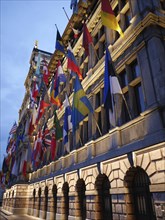 European building with many flags, illuminated at dusk, the historic market square of Antwerp at