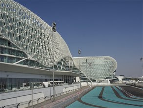Modern building with striking grid structure and adjacent race track under blue skies, Abu Dhabi,