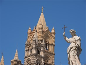 Large cathedral building with gothic tower and a statue holding a cross, palermo in sicily with an