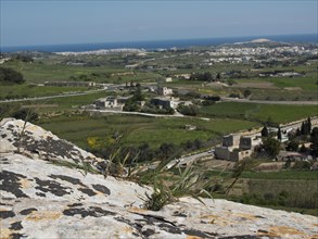Landscape with hills, fields, individual buildings and the sea in the background, the town of mdina