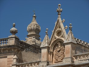 A historic building with gothic details and a tower under a blue sky, the town of mdina on the