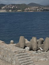 Coastline with concrete breakwaters and a view over the sea to a town and hills, Corsica, ajaccio,