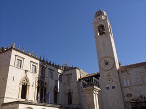 Square with historic tower, gothic facades and flags under a clear blue sky, the old town of