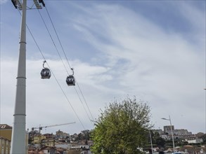 Cable car gondolas crossing a tree, houses and cable car support in the background, cloudy sky,