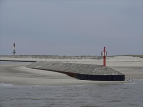 Red beacon on a gravel embankment along the coast with sand dunes and grey sky, buhne on an island