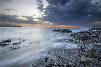 Sunrise with sea view on a rocky coast in warm colours. Landscape with a lava stone beach of