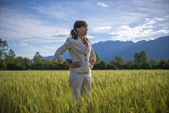 Proud and elegant Woman with Her Hands on Her Hips Standing on a Wheat Field with Mountain in the