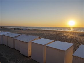 White beach huts on the beach with a view of the sunset and the sea, sunset in many colours on the