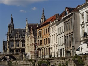A city view with historic buildings and gothic towers along a canal under a blue sky, medieval
