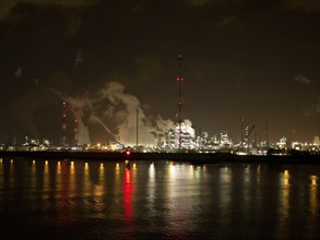 Illuminated industrial buildings and plants at night, their lights reflected in the water,