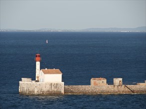 White lighthouse with red roof on a wall in the sea with a calm coastal landscape, la seyne sur