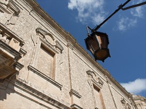 View of historic stone wall with street lamp against a blue sky, the town of mdina on the island of