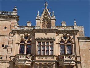 Magnificent facade with ornate windows and balconies and a magnificent coat of arms under a bright