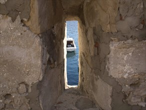 View through a narrow gap in an old stone wall to a boat in the sea, the old town of Dubrovnik with