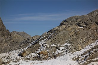 Stony and snowy mountain landscape with scattered rock formations under a clear sky, bare mountain