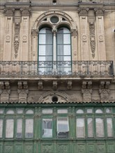 A historic facade with ornate windows and a balcony harmonises with the lower green cladding,