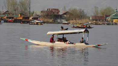 People on a boat in a serene lake with rustic houses and trees in the background