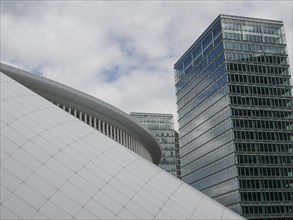 White arched structure in front of modern skyscrapers and glass facades under a cloudy sky, modern