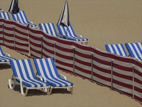 Close-up of blue and white striped deckchairs and umbrellas on clean sandy beach, colourful beach