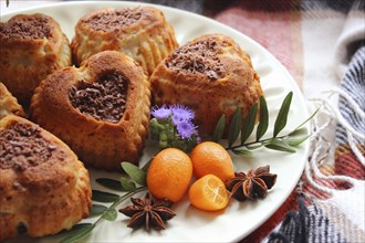 Heart-shaped cakes adorned with kumquats, star anise, and a purple flower on a plate with a