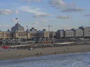 A view of a large city with historic and modern buildings on the beach, some people, a flag and a