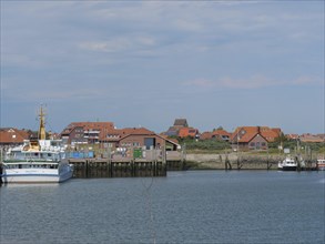 View of a harbour with several ships and houses behind them under a slightly cloudy sky, Baltrum