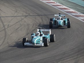 Two racing cars take a bend on a race track, both drivers wear helmets, Abu Dhabi, Arab Emirates