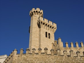 Historic castle tower with battlements and a stone wall in front of a clear blue sky, palma de