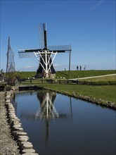 A historic windmill is reflected in a small canal on a clear day, Enkhuizen, Nirderlande