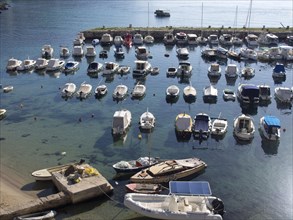 A sunny harbour full of boats bobbing in the clear water, with a pier in the foreground, the old