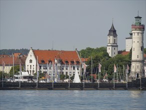Town view with historical buildings, lighthouse and sailing boats on the calm water, towers at a