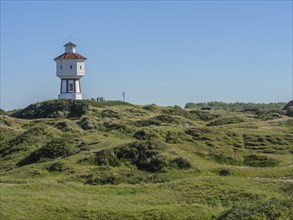 A lighthouse rises out of a vast grassy landscape under a clear blue sky, the atmosphere is calm,