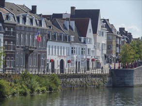 Rows of old town houses along the river under a clear sky with a visible flag, Maastricht,