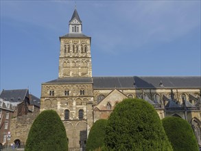 Historic church with a central tower and green bushes in the foreground, against a blue sky,