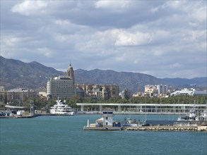 View of a harbour with buildings in the background and mountains behind, the sky is cloudy, spring