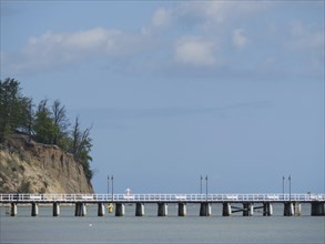 A pier next to a cliff with trees stretching into the sea under a cloudy sky, spring on the Baltic