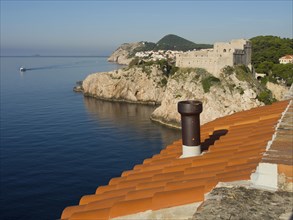 Red roof tiles with a view of the blue sea and an old castle on a hill, the old town of Dubrovnik