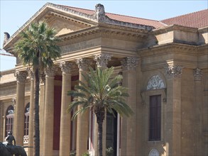 A neoclassical building with large stone columns and palm trees in front, palermo in sicily with an