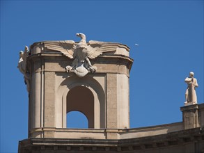Close-up of a building tower decorated with sculptures and an eagle under a clear blue sky, palermo