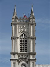 A Gothic church tower with detailed decorations and a flag against a blue sky, London, England,