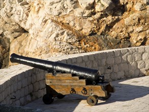 Black cannon on a wooden frame in front of a historic stone wall, the old town of Dubrovnik with