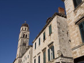 Bell tower and buildings with green shutters against a bright blue sky, the old town of Dubrovnik