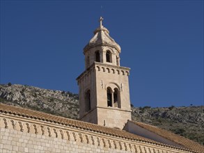 Historic stone church tower, in the background hills under a clear blue sky, the old town of