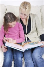 Mother and daughter sitting in living room reading book