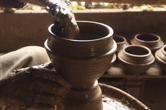 Hands shaping clay on a pottery wheel, creating multiple pottery items, emphasizing the art of