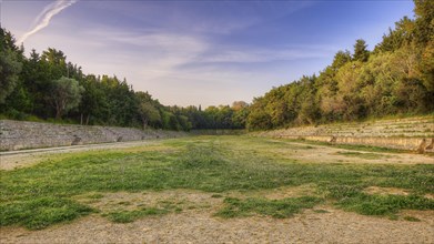 Stadium of Rhodes, Ancient ruins surrounded by a green meadow and trees at sunrise, with a clear,