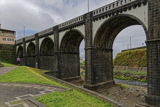 Historic eight-arched bridge over the Ribeira Grande River, surrounded by grasslands, under a