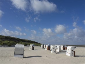 Various beach chairs standing on a sandy beach under a blue sky with some clouds, Spiekeroog,